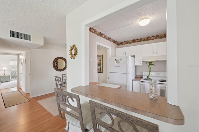 7304 W Country Club Dr N Unit 113, Sarasota, FL 34243 - kitchen with white appliances, a textured ceiling, under cabinet range hood, white cabinetry, and light wood-style floors