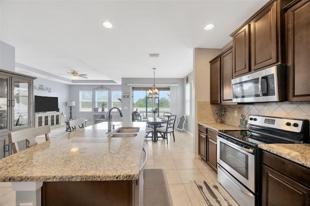 5624 Fisher Glen Loop, Wesley Chapel, FL 33545 - kitchen with stainless steel appliances, a sink, tasteful backsplash, light stone countertops, and an island with sink