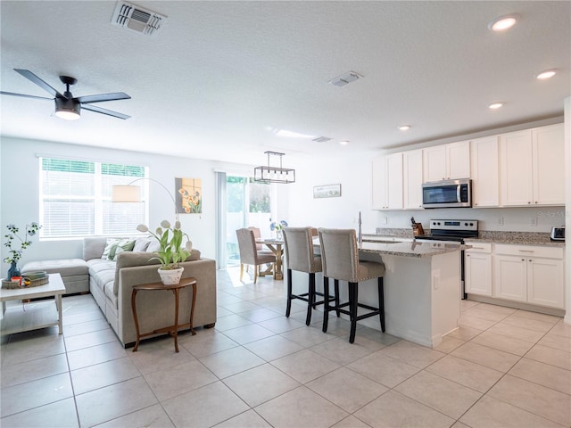 573 Vista Villages Blvd, Davenport, FL 33896 - kitchen with stainless steel appliances, white cabinetry, light stone countertops, a breakfast bar, and light tile patterned floors