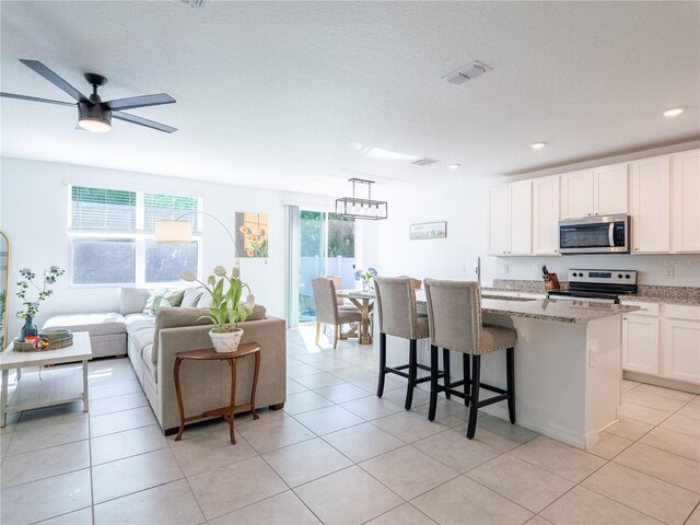 573 Vista Villages Blvd, Davenport, FL 33896 - kitchen featuring appliances with stainless steel finishes, light stone countertops, a kitchen island, white cabinetry, and a ceiling fan