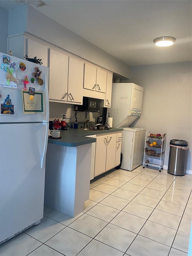 3802 Cortez Cir Unit D, Tampa, FL 33614 - kitchen with freestanding refrigerator, stacked washing machine and dryer, white cabinetry, dark countertops, and light tile patterned floors