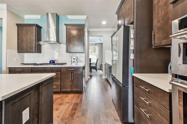 14110 Barrington Stowers Dr, Lithia, FL 33547 - kitchen with wall chimney exhaust hood, appliances with stainless steel finishes, crown molding, hardwood / wood-style flooring, and light countertops