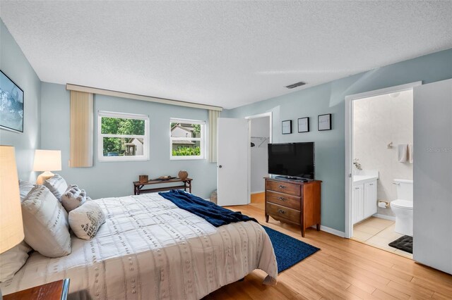 1400 Tarpon Woods Blvd Unit A4, Palm Harbor, FL 34685 - bedroom featuring light wood-type flooring, a textured ceiling, a walk in closet, and connected bathroom