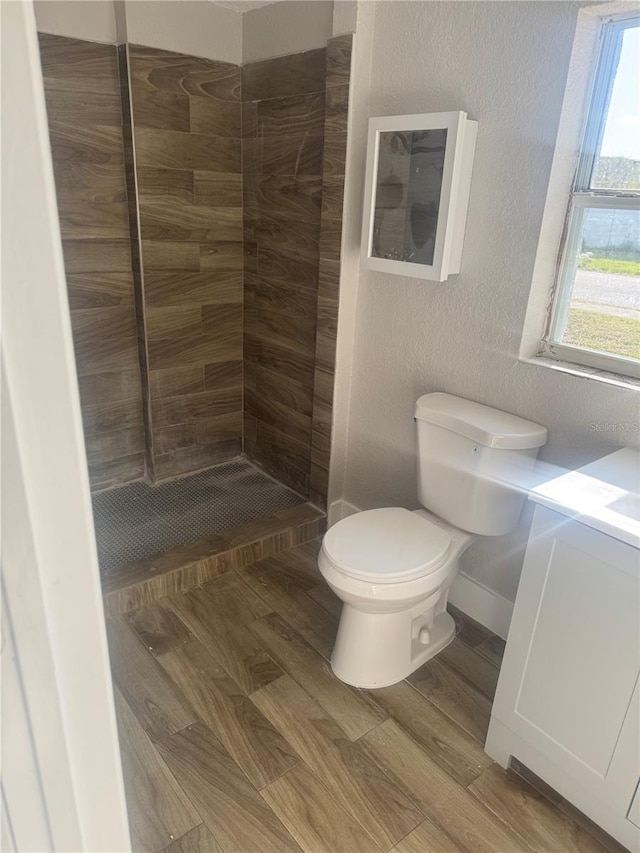 8502 Grapefruit Ave, Tampa, FL 33619 - bathroom featuring toilet, a tile shower, vanity, wood finished floors, and a textured wall