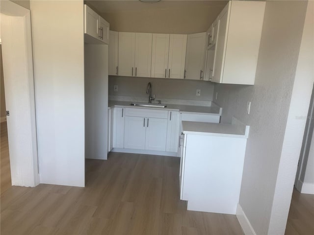 8502 Grapefruit Ave, Tampa, FL 33619 - kitchen with a sink, light wood-style flooring, light countertops, and white cabinets