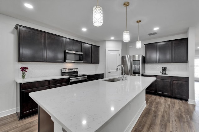 6658 Devlin Ln, Wesley Chapel, FL 33545 - kitchen featuring stainless steel appliances, a sink, backsplash, wood finished floors, and a center island with sink