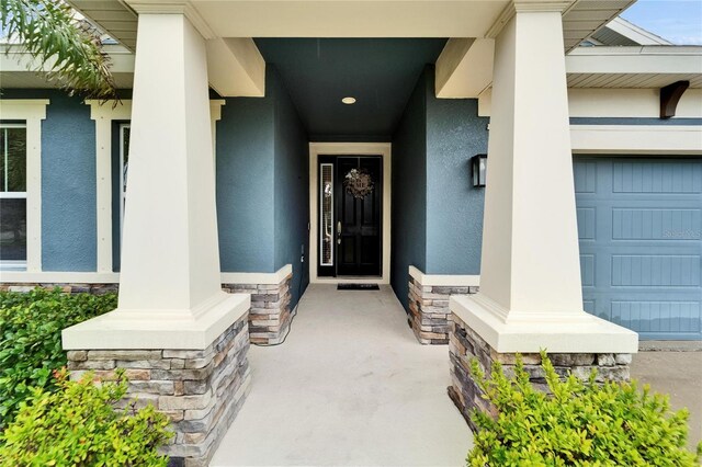6127 Colmar Pl, Apollo Beach, FL 33572 - doorway to property featuring stucco siding, covered porch, stone siding, and a garage