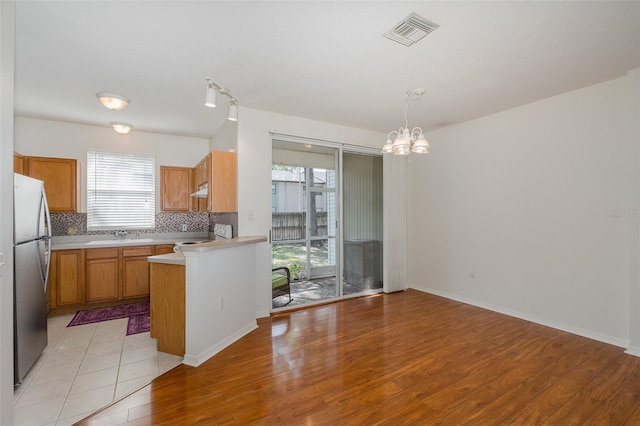 13521 Forest Lake Dr, Largo, FL 33771 - kitchen with freestanding refrigerator, a chandelier, light wood finished floors, light countertops, and tasteful backsplash