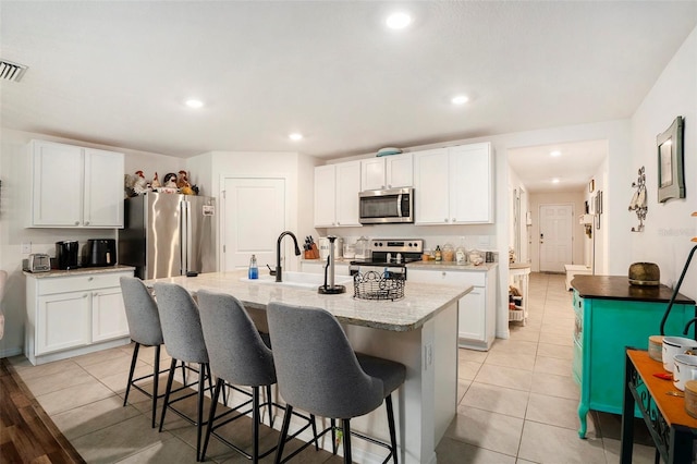 7639 Broad Pointe Dr, Zephyrhills, FL 33540 - kitchen featuring appliances with stainless steel finishes, a kitchen breakfast bar, white cabinetry, an island with sink, and light tile patterned flooring