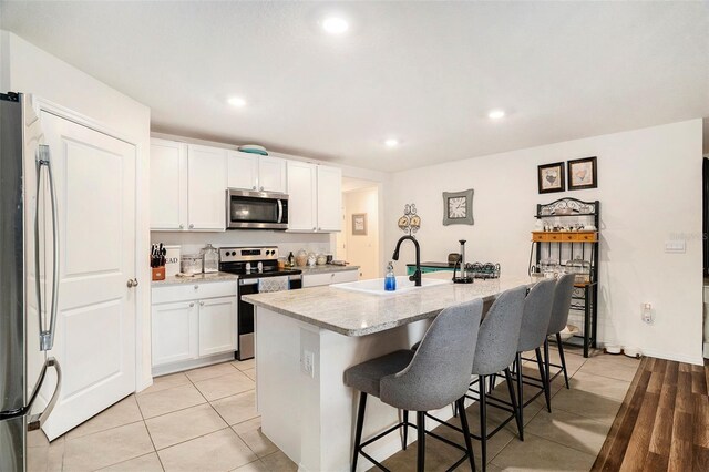 7639 Broad Pointe Dr, Zephyrhills, FL 33540 - kitchen featuring appliances with stainless steel finishes, a center island with sink, a breakfast bar, white cabinetry, and light tile patterned floors