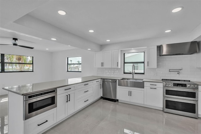 319 Midway Is, Clearwater Beach, FL 33767 - kitchen with appliances with stainless steel finishes, a sink, a peninsula, wall chimney range hood, and decorative backsplash