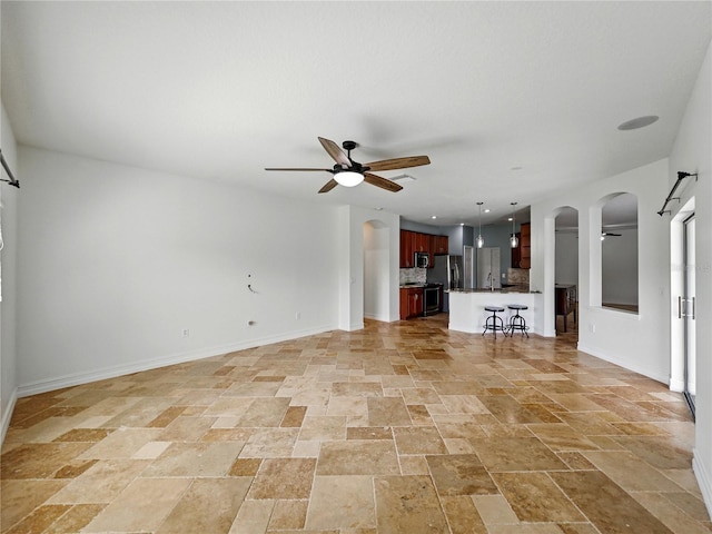 6957 Boulder Run Loop, Wesley Chapel, FL 33545 - unfurnished living room with ceiling fan, stone tile flooring, arched walkways, and baseboards