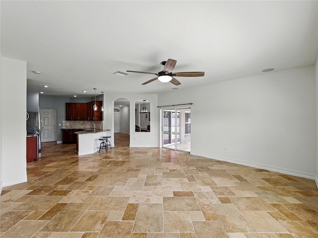 6957 Boulder Run Loop, Wesley Chapel, FL 33545 - unfurnished living room featuring arched walkways, ceiling fan, stone tile flooring, baseboards, and recessed lighting