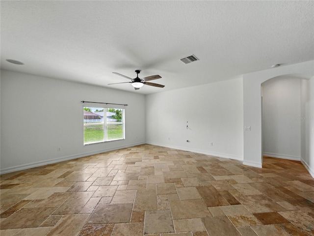 6957 Boulder Run Loop, Wesley Chapel, FL 33545 - empty room featuring arched walkways, stone tile floors, ceiling fan, a textured ceiling, and baseboards