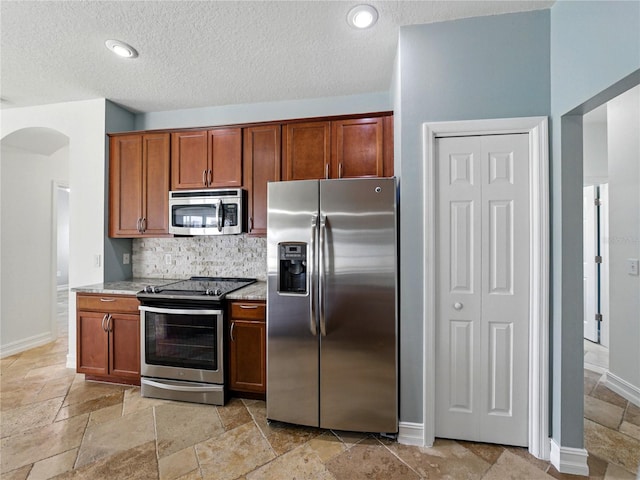 6957 Boulder Run Loop, Wesley Chapel, FL 33545 - kitchen with appliances with stainless steel finishes, arched walkways, stone tile floors, decorative backsplash, and a textured ceiling