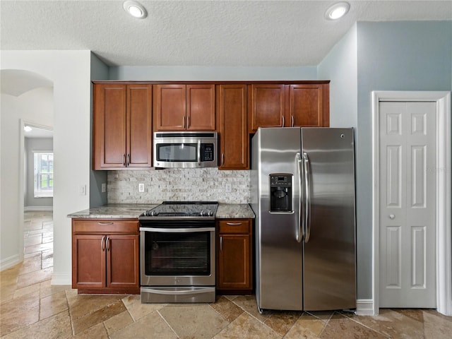 6957 Boulder Run Loop, Wesley Chapel, FL 33545 - kitchen featuring appliances with stainless steel finishes, arched walkways, tasteful backsplash, stone tile floors, and light stone countertops