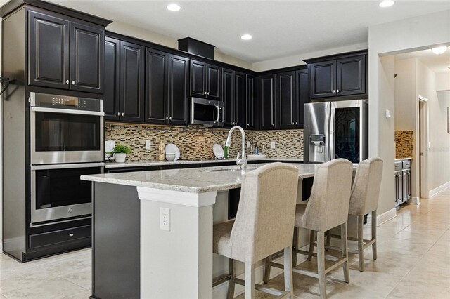 18696 Malinche Loop, Spring Hill, FL 34610 - kitchen featuring stainless steel appliances, dark cabinetry, an island with sink, light stone countertops, and recessed lighting