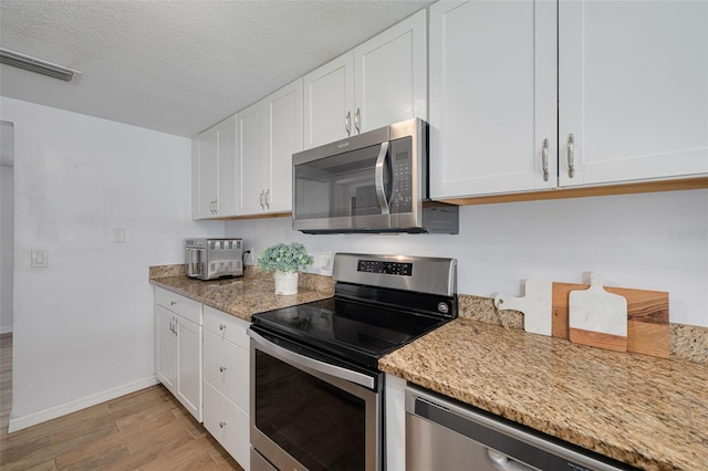 8014 Lotus Dr, Port Richey, FL 34668 - kitchen with appliances with stainless steel finishes, light wood-style floors, white cabinets, light stone counters, and a textured ceiling