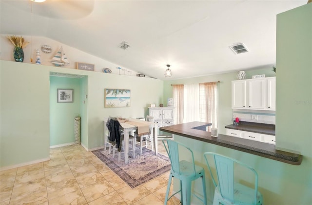3312 Holly Springs Dr, Hernando Beach, FL 34607 - kitchen featuring dark countertops, lofted ceiling, white cabinetry, a peninsula, and a kitchen breakfast bar