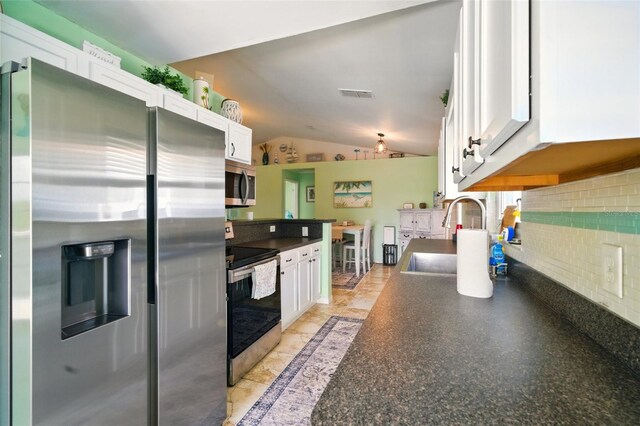 3312 Holly Springs Dr, Hernando Beach, FL 34607 - kitchen featuring stainless steel appliances, a sink, vaulted ceiling, white cabinets, and dark countertops