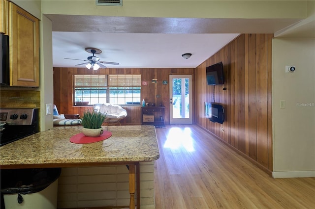 18121 Geraci Rd, Lutz, FL 33548 - kitchen with wood walls, light wood-type flooring, brown cabinetry, ceiling fan, and stainless steel range oven