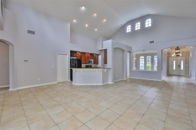 7114 Cromwell Park Ln, Apollo Beach, FL 33572 - unfurnished living room featuring light tile patterned floors, high vaulted ceiling, a chandelier, arched walkways, and baseboards