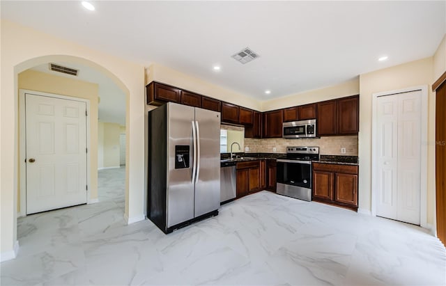 3305 Hoylake Ct, Land O Lakes, FL 34638 - kitchen featuring appliances with stainless steel finishes, arched walkways, decorative backsplash, dark countertops, and light marble finish floors