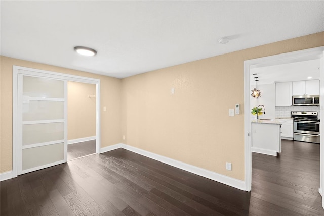 3906 W Rogers Ave, Tampa, FL 33611 - empty room with dark wood-style floors, baseboards, a sink, and a smoke detector