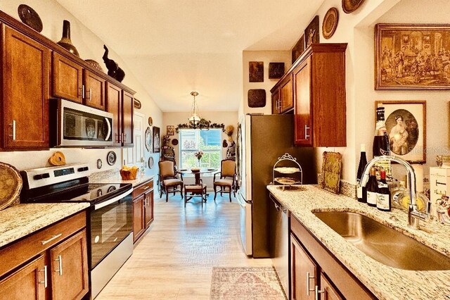 5103 98th Ave E, Parrish, FL 34219 - kitchen with appliances with stainless steel finishes, a sink, light stone counters, light wood-style flooring, and pendant lighting