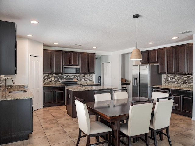 kitchen featuring stainless steel appliances, decorative backsplash, light tile patterned floors, a center island, and dark brown cabinetry