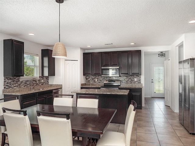 kitchen featuring stainless steel appliances, a textured ceiling, decorative backsplash, a kitchen island, and light tile patterned floors