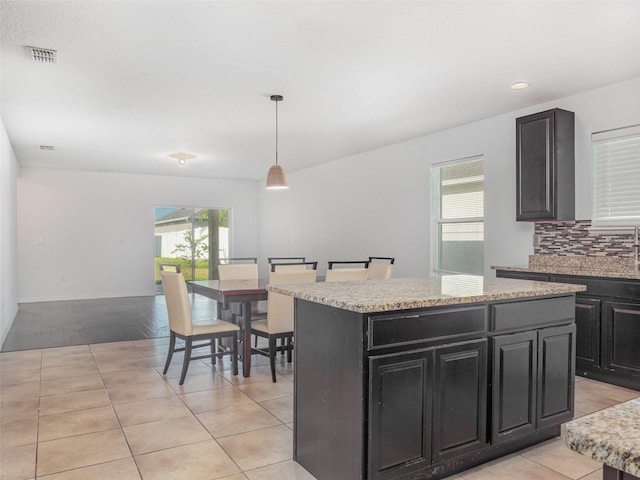 kitchen with dark cabinetry, light tile patterned floors, a kitchen island, decorative light fixtures, and tasteful backsplash