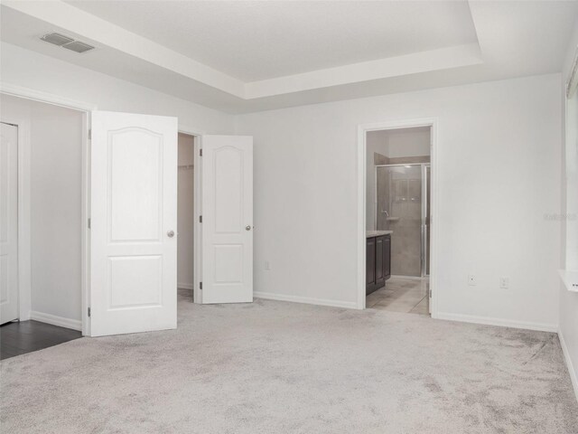 unfurnished bedroom with light colored carpet, a raised ceiling, and ensuite bathroom