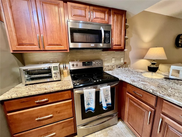 2131 Ridge Rd S Unit 76, Largo, FL 33778 - kitchen with stainless steel appliances, decorative backsplash, brown cabinetry, and light stone counters