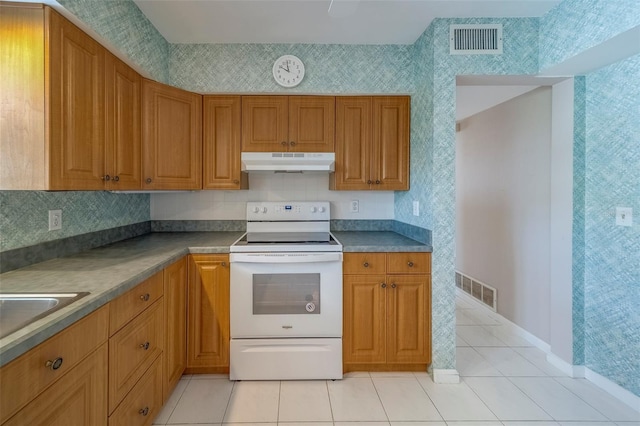 501 Poinsettia Rd, Belleair, FL 33756 - kitchen with under cabinet range hood, electric stove, light tile patterned flooring, brown cabinets, and wallpapered walls