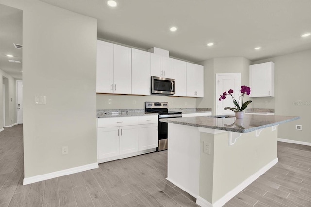 3146 Forrest Plum Ct, Zephyrhills, FL 33540 - kitchen with stainless steel appliances, light wood-style flooring, baseboards, an island with sink, and dark stone counters