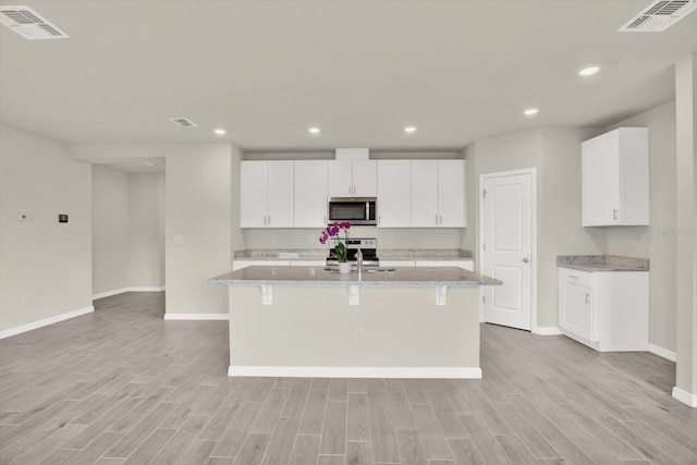 3146 Forrest Plum Ct, Zephyrhills, FL 33540 - kitchen with stainless steel appliances, baseboards, light wood-style floors, an island with sink, and white cabinetry