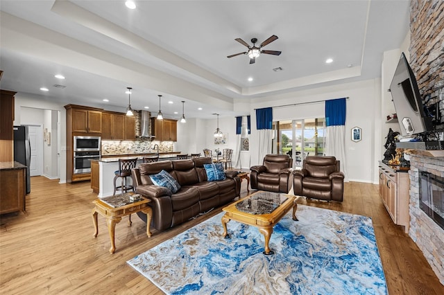 33219 Kateland Dr, Wesley Chapel, FL 33545 - living room featuring a tray ceiling, a fireplace, a ceiling fan, light wood-type flooring, and recessed lighting