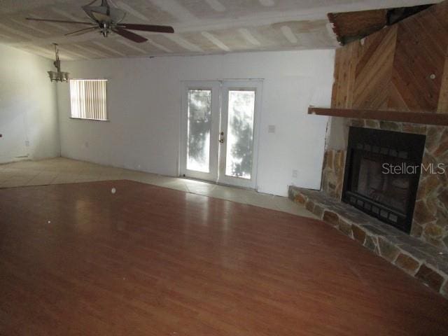 5190 Starling Dr, Mulberry, FL 33860 - unfurnished living room featuring wood finished floors, ceiling fan, a stone fireplace, french doors, and a chandelier