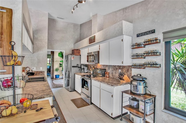 12219 Steppingstone Blvd, Tampa, FL 33635 - kitchen with stainless steel appliances, a sink, a towering ceiling, light tile patterned floors, and white cabinetry