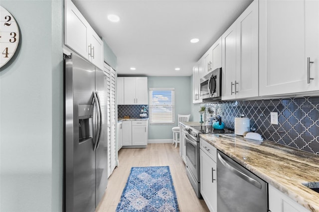 12525 3rd St E Unit 303, Treasure Island, FL 33706 - kitchen featuring stainless steel appliances, light wood finished floors, tasteful backsplash, white cabinets, and light stone counters