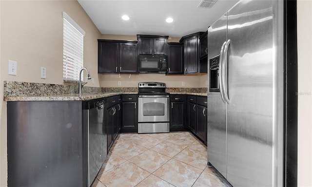 9752 Trumpet Vine Loop, Trinity, FL 34655 - kitchen with stainless steel appliances, a sink, light stone counters, light tile patterned floors, and dark cabinetry