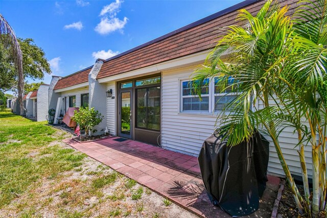 9142 Oakwood Ln, Seminole, FL 33776 - view of exterior entry with a patio, a yard, mansard roof, and a shingled roof