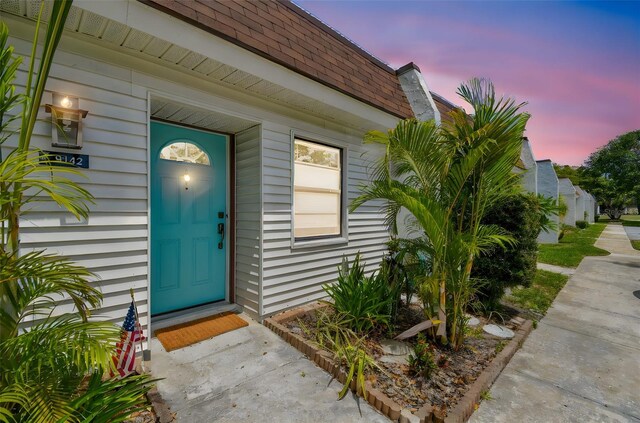 9142 Oakwood Ln, Seminole, FL 33776 - exterior entry at dusk featuring roof with shingles and mansard roof