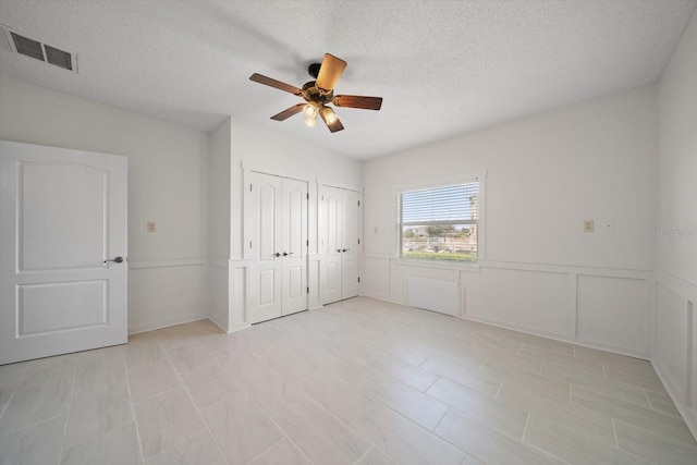 3397 Bluefish Dr, Hernando Beach, FL 34607 - unfurnished bedroom featuring two closets, a textured ceiling, a ceiling fan, and a wainscoted wall