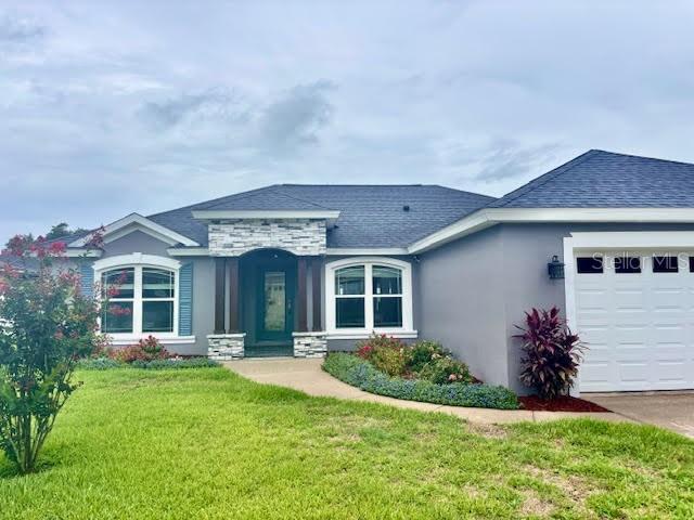 7144 Remington Oaks Loop, Lakeland, FL 33810 - view of front facade featuring stucco siding, a front yard, an attached garage, stone siding, and a shingled roof