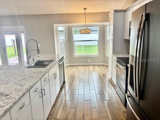 7144 Remington Oaks Loop, Lakeland, FL 33810 - kitchen with stainless steel appliances, a sink, light wood finished floors, white cabinetry, and decorative light fixtures
