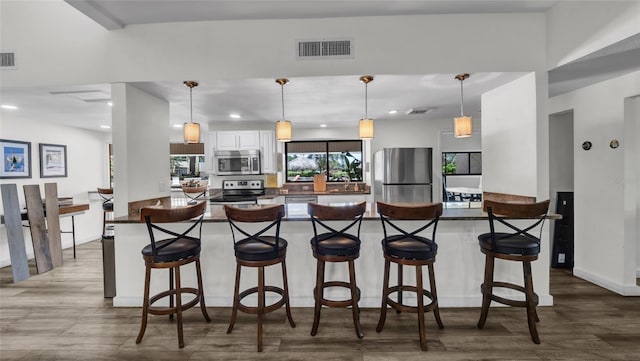 2616 Cove Cay Dr Unit 505, Clearwater, FL 33760 - kitchen with appliances with stainless steel finishes, dark countertops, wood finished floors, a kitchen bar, and white cabinetry