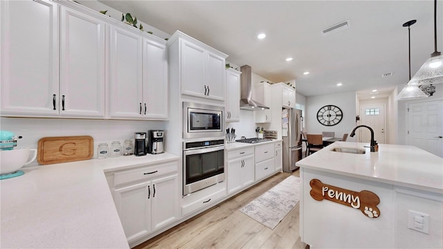5645 Del Coronado Dr, Apollo Beach, FL 33572 - kitchen with stainless steel appliances, a sink, wall chimney exhaust hood, white cabinets, and light wood-type flooring