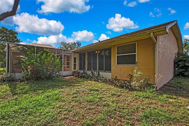6121 Piedmont Dr, Spring Hill, FL 34606 - rear view of house with glass enclosure, stucco siding, and a lawn